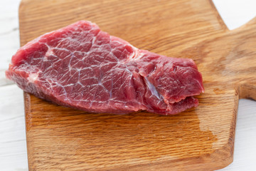 Morning in the kitchen. Raw meat. Raw fresh beef steak on a wood cutting board. White wooden background, top view, copy space, Daylight