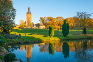 Ancient church on the edge of a pond along trees below a blue sky in sunlight at fall