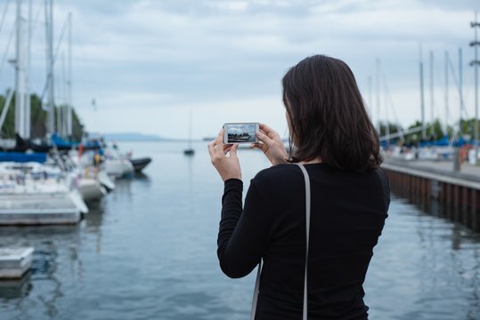 Woman clicking photos with mobile phone near harbor