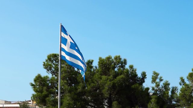 Torn old greek flag wave on beach agains blue sky