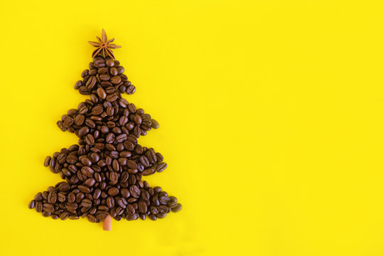 Winter composition with Christmas tree made by coffee beans and decorated anise star and cinnamon stick on a yellow background, flat lay. Greeting card for New Year with copy space.