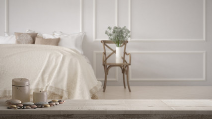 Wooden vintage table top or shelf with candles and pebbles, zen mood, over blurred vintage classic bedroom with soft bed full of pillows and blankets, minimal architecture interior design