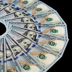 One hundred dollar bills are fanned out on a black background. Top side view.