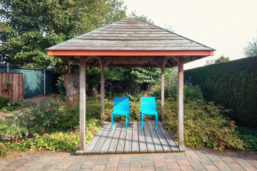 Two blue chairs under an arbor to enjoy the sun in the corner of a beautiful autumn garden