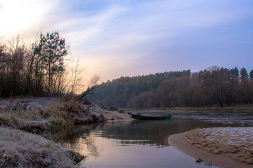 landscape by the river: a wooden boat at the shore and the first frost