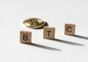 BTC bitcoin with letter tiles on white casting shadows.