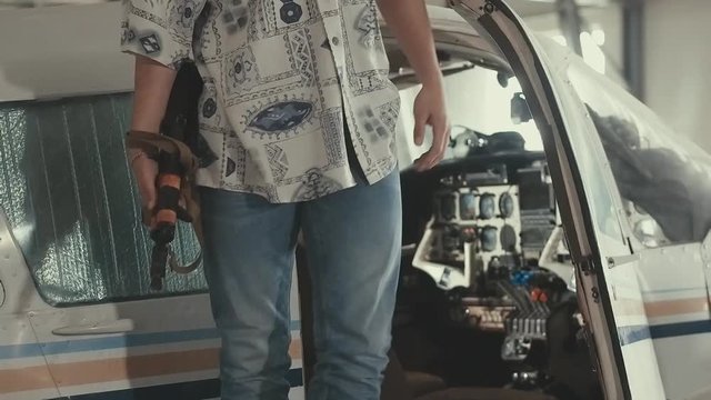 Colombian gangster in a white shirt in the style of the 80s stands near the plane and checks the quality of cocaine or other drugs, is holding a machine gun, very serious, incredulous
