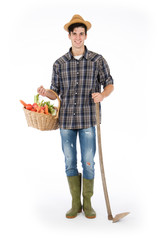 Young farmer holding one arm holding a basket with fruit and vegetables, with the other a hoe, he is wearing a straw hat, checked shirt and green rubber boots