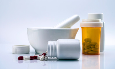 Capsules red and white out of a bottle next to mortar pharmacist, conceptual image