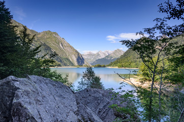 Two small rocks in front of the magnificent landscape of the French mountains and a clear blue mountain lake.