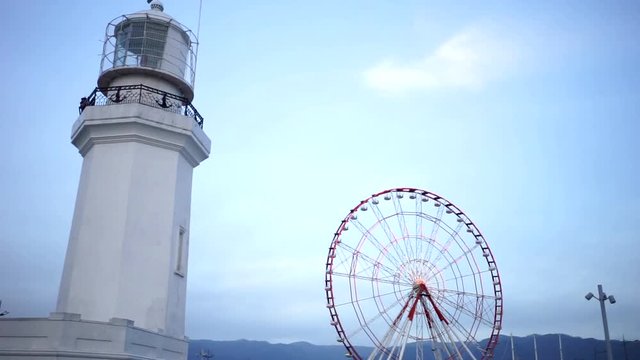 Lighthouse shines on the beach. Lighthouse next to the Ferris wheel. Ferris wheel in the amusement Park. Rest in the amusement Park. Lighthouse at sunset tonight.