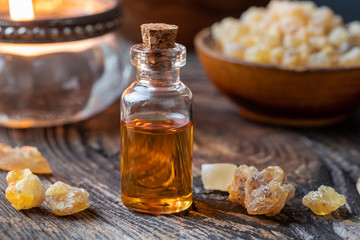 A bottle of frankincense essential oil with frankincense crystals and a candle