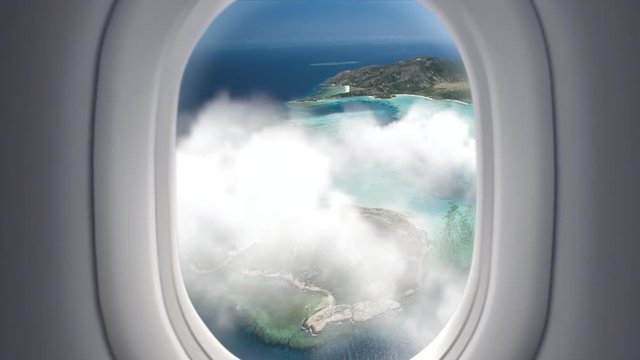 View from the window at passenger seat in airplane flight above clouds and sea with tropical islands