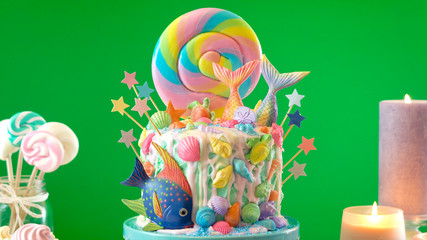 Mermaid theme candyland cake with colorful glitter tails, shells and sea creatures toppers for children's, teen's, novelty birthday and party celebrations, green background.