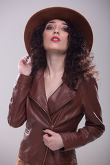 portrait of a beautiful girl in a brown leather jacket and hat on white background