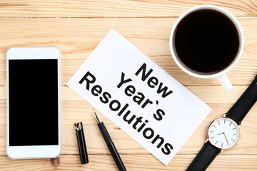 New year resolutions on sheet of paper with smartphone, wrist watch and cup of coffee