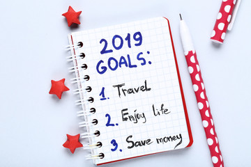 Inscription 2019 goals in notepad with pen and paper stars on grey background