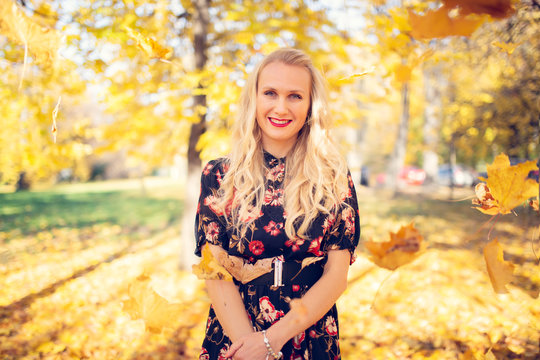Image of smiling woman in dress on blurred background of autumn park