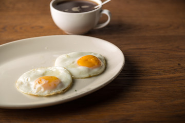Fried Eggs on white plate and cup of black Coffee for Breakfast on wooden background