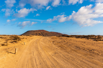 Fototapeta na wymiar Scenic view of a golden sand road leading through a volcanic landscape on a hot and sunny day. La Graciosa island in Canary, Spain.