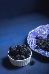 Fototapeta na wymiar food photo of blackberries on blue dark rustic background, in white bowl, minimalistic food photo