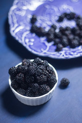blackberries in white bowl on dark blue background, food photo
