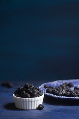 white bowl of blackberries on blue dark rustic background