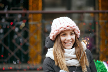 Merry blonde model wearing winter outfit celebrating Christmas at the street with sparklers. Space for text