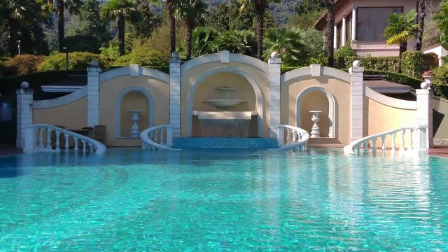 Static footage of classic swimming pool showing the fresh blue water without people in it and also the decorative wall with marble additions at the back of the piscine 4k high resolution video