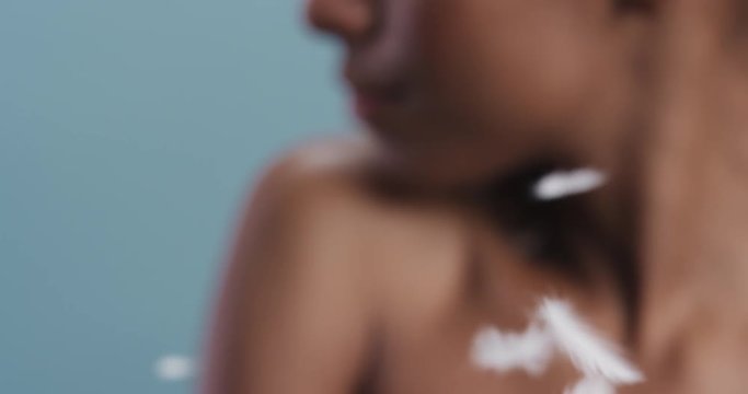 close up beauty portrait attractive african american woman feathers falling on smooth skin touching bare shoulders enjoying natural skincare gently caressing body in blue background slow motion