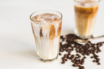 Ice coffee in a glass with cream over and coffee beans on the table