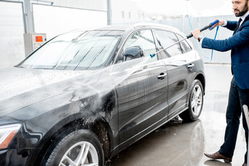 Businessman dressed in the suit washing his luxury car with washing gun on a self service open air car wash