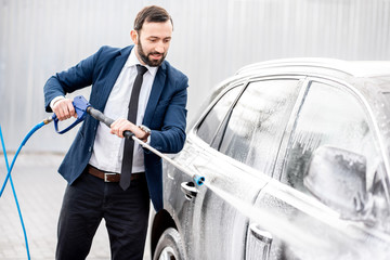 Businessman dressed in the suit washing his luxury car with washing gun on a self service open air car wash