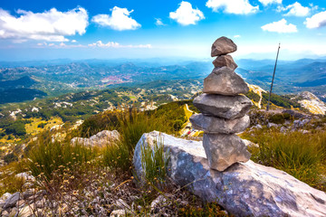 Stone cairns pyramid built on top of a mountain with a panoramic view of the Montenegrin valley of hills and forests under a blue sky with white clouds. Vidikovac, Lovcen National Park, Montenegro.
