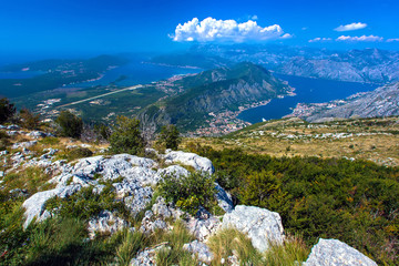 Panoramic view from the stone top of the mountain on the gulf and houses in the city between the mountains, hillsides in the grass and green trees. Aerial view of Kotor, Boka Kotorska Bay, Montenegro.