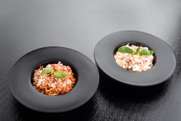 spaghetti bolognese and fetuchini carbonara decorated with basil in a black plates isolated on a dark background. close up. space.