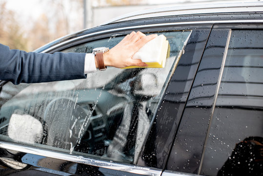 Businessman Washing Car Window With Sponge And Foam On A Self Service Car Wash, Close-up View With Reflection On The Window