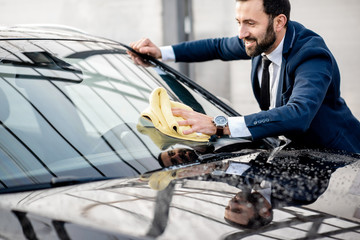 Smiling businessman dressed in a suit wiping windshield of his car with yellow microfiber on a self service car wash outdoors