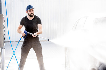 Professional washer in black uniform washing luxury car with water gun on an open air car wash