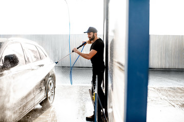 Professional washer in black uniform washing luxury car with water gun on an open air car wash