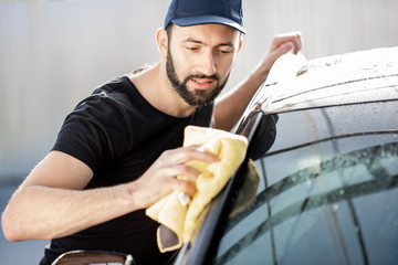 Professional washer wiping a car window with yellow sponge, washing luxury car outdoors