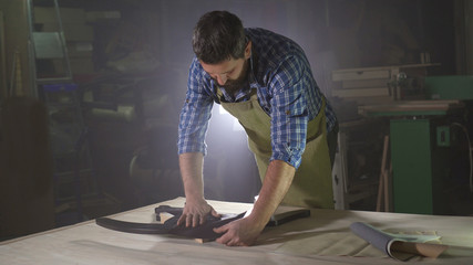 male kraftman with a beard in a dark workshop with a sample of leather for making furniture