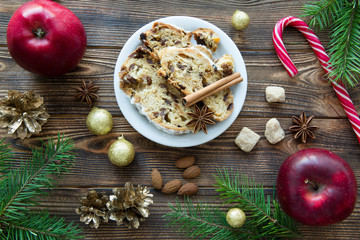 Traditional Christmas stollen cake with raisins and nuts. German dessert on brown wooden table background. Red apples, christmas candy stick.