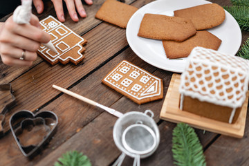 Icing of Christmas bakery. Woman decorating honey gingerbread cookies on wooden brown table....