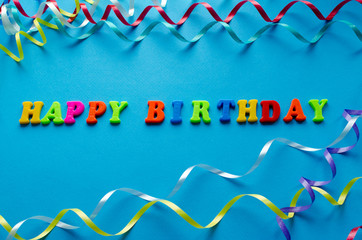 Happy birthday text from colored plastic magnets on blue paper background.