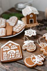 A lot of ginger biscuits in different form on brown wooden table. Decorated with white sweet glaze. Christmas mood, winter morning. Fir branches and forms for baking