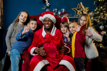Beautiful young children laughing, hugging African Santa Claus, waving their hands