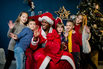 Beautiful young children laughing, hugging African Santa Claus, waving their hands