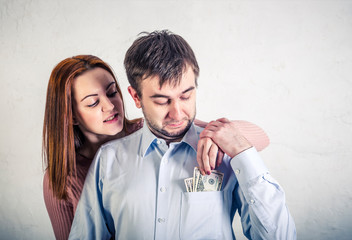 young wife pulls out dollar bills from her husband's shirt pocket, the husband grabbed her hand and does not allow to pull out the money.