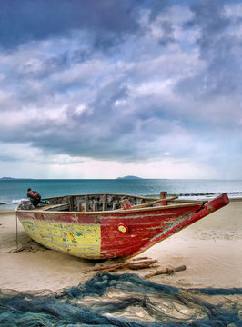 Old colorful wooden fisherboat on an overcast beach, Sanya, China.